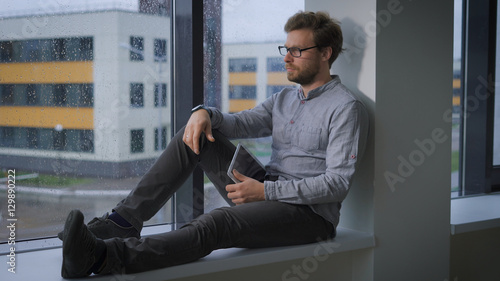 Pensive young man sitting at window.