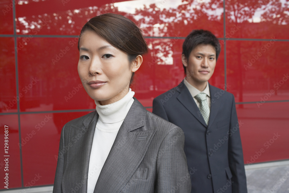 Portrait of two confident businesspeople standing against red building Portrait of two confident businesspeople standing against red building