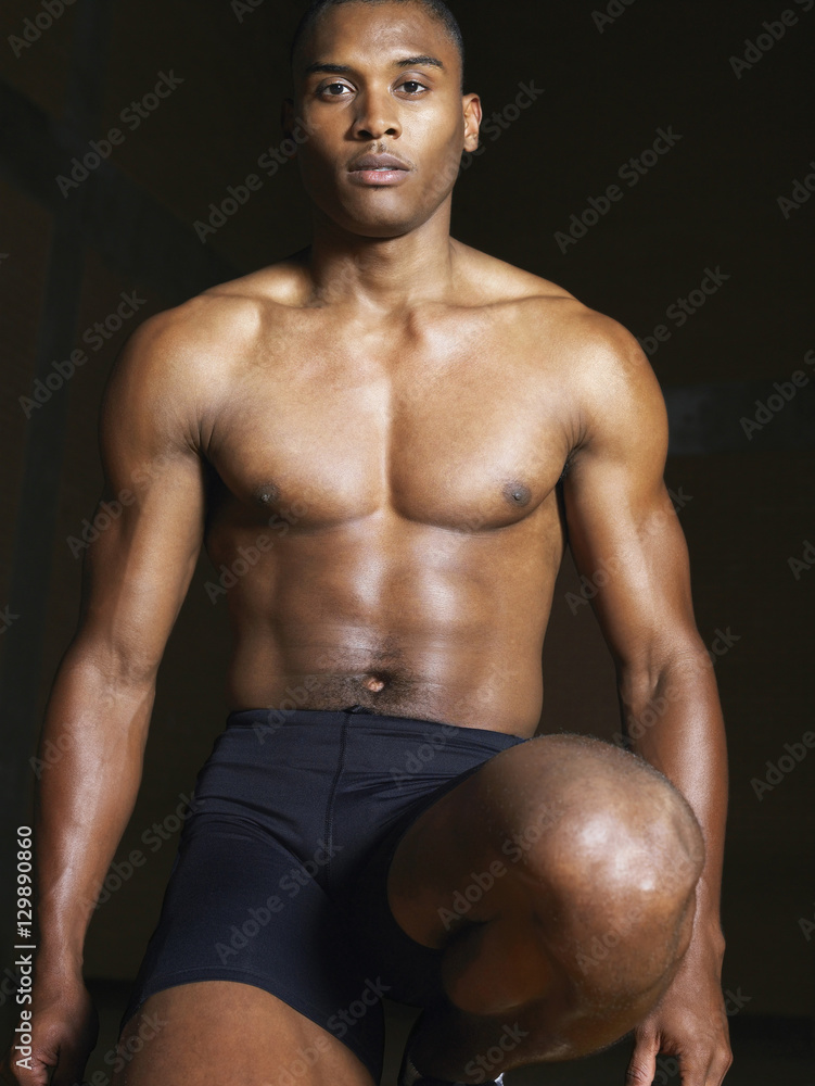 Fototapeta premium Portrait of a bare chested runner kneeling down against dark background
