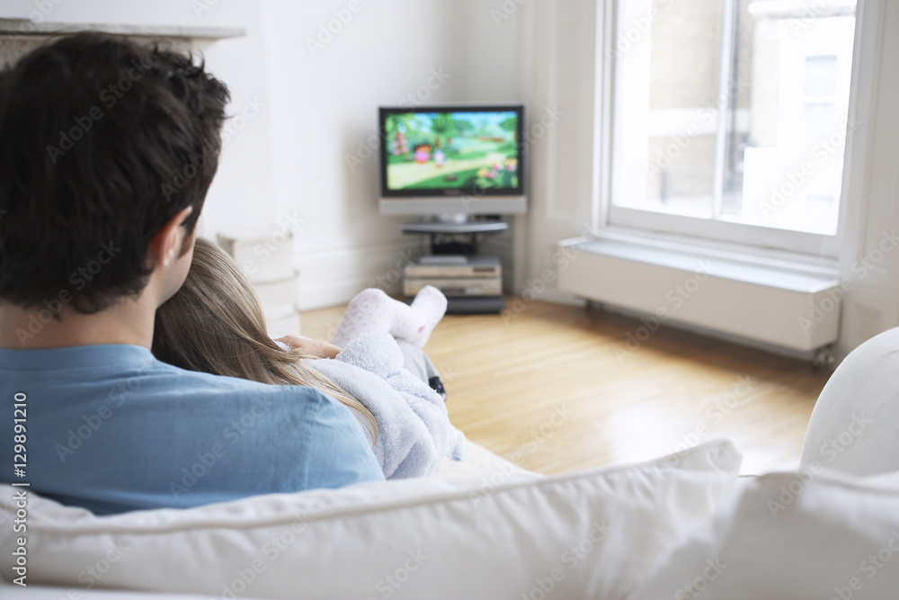 Closeup rear view of father and daughter watching cartoons in television at home Closeup rear view of father and daughter watching cartoons in television at home