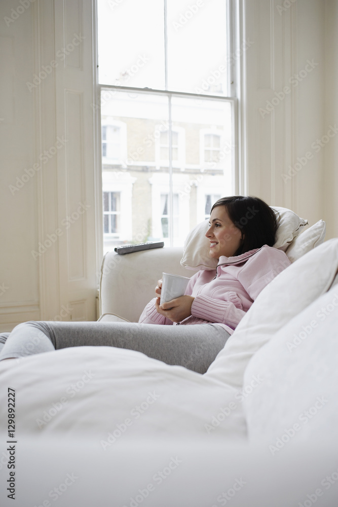 Young woman lying on couch with coffee cup at home Young woman lying on couch with coffee cup at home
