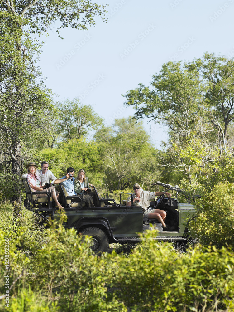 Fototapeta premium Side view of four tourists and driver in jeep on safari 