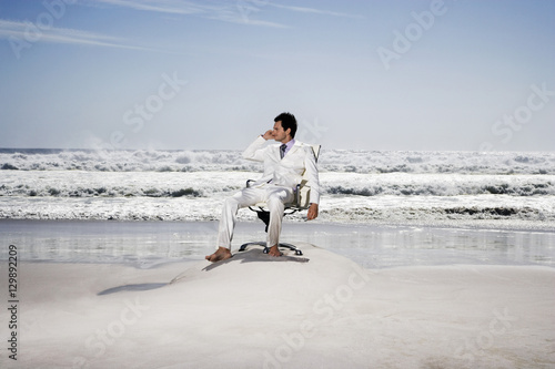 Full length of businessman using cellphone on office chair at beach