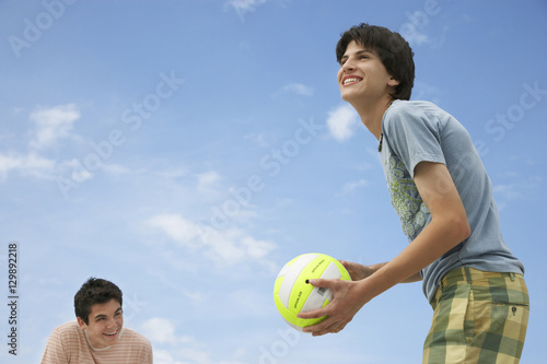 Low angle view of happy teenage boys playing beach volleyball against sky © moodboard