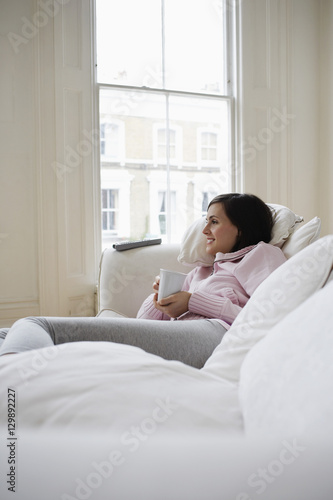 Young woman lying on couch with coffee cup at home