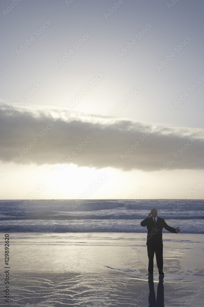 Middle aged businessman using cell phone in sea at sunset Middle aged businessman using cell phone in sea at sunset