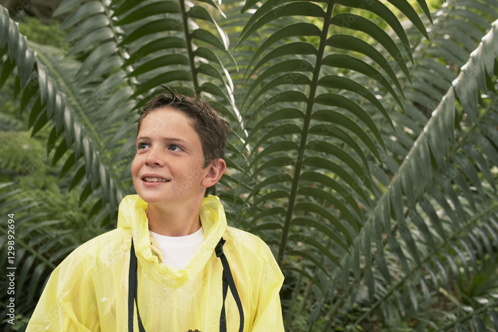 Young boy in raincoat standing in front of large fern during field trip Young boy in raincoat standing in front of large fern during field trip