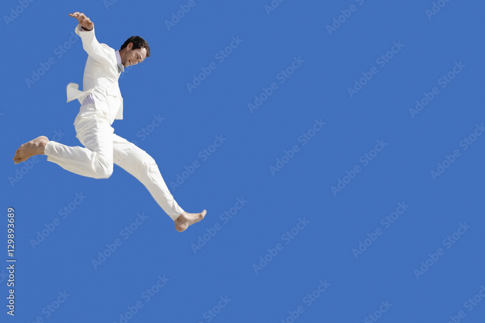 Full length of young businessman jumping against blue sky Full length of young businessman jumping against blue sky