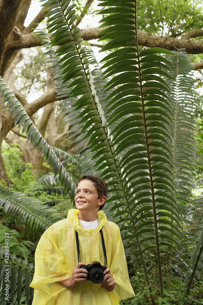 Young boy with camera standing by large fern in forest during field trip Young boy with camera standing by large fern in forest during field trip