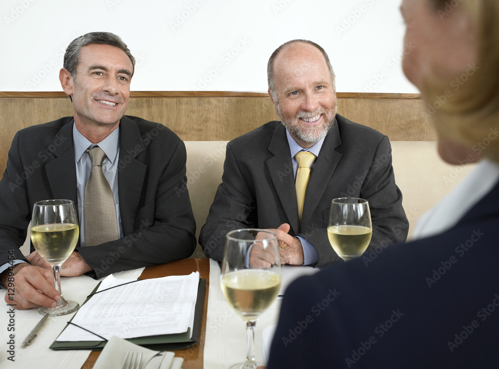 Middle aged business people with wineglasses and documents discussing in restaurant