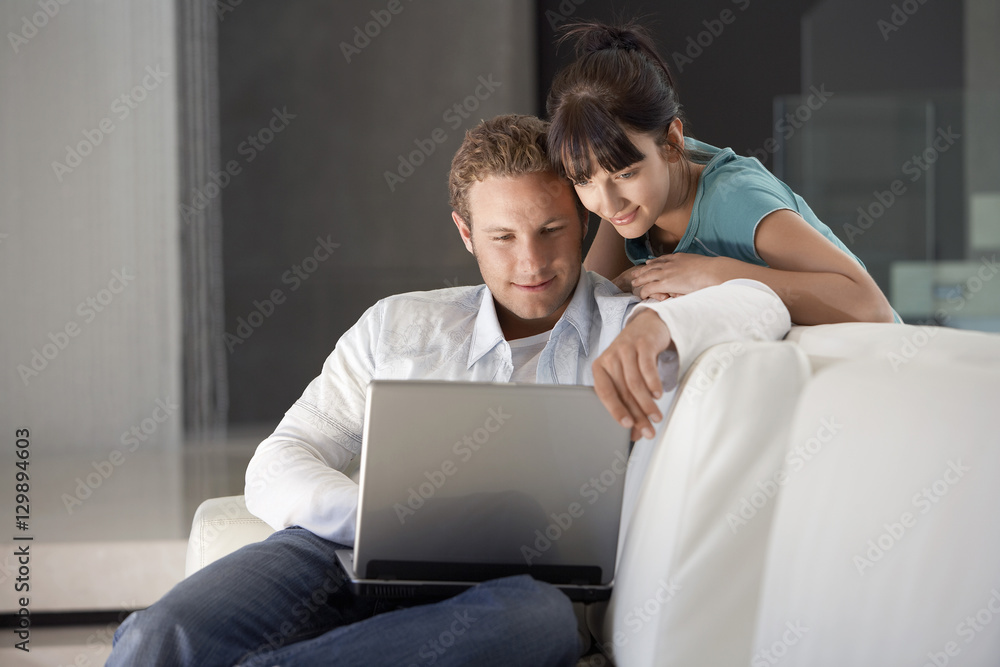 Happy young couple using laptop on sofa in living room Happy young couple using laptop on sofa in living room