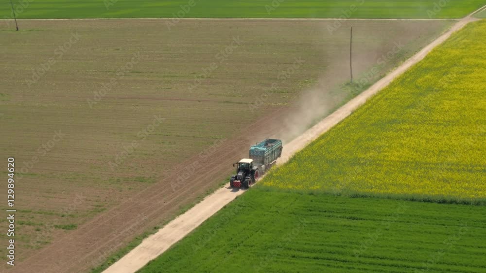 AERIAL: Tractor driving on dusty country road between colorful crop fields AERIAL: Tractor driving on dusty country road between colorful crop fields