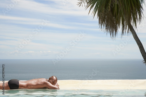 Young African American man relaxing by poolside with ocean in background