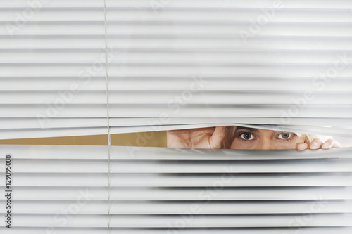 Canvas Print Young woman looking through Venetian blinds