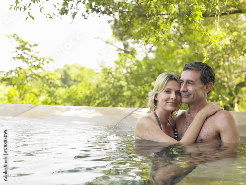 Smiling adult couple embracing in swimming pool against trees