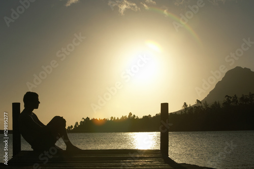 Side view of man sitting on dock by lake enjoying sunset photo