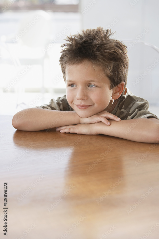 Thoughtful young boy leaning on wooden dining table Thoughtful young boy leaning on wooden dining table