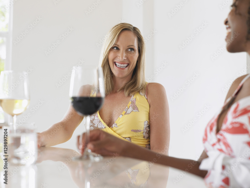 Two cheerful multiethnic women with red and white wine sitting at the table