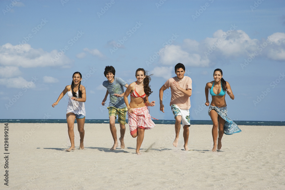 Full length of happy teenage friends running on sandy beach