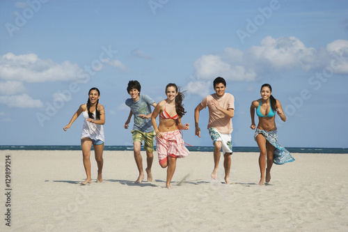 Full length of happy teenage friends running on sandy beach