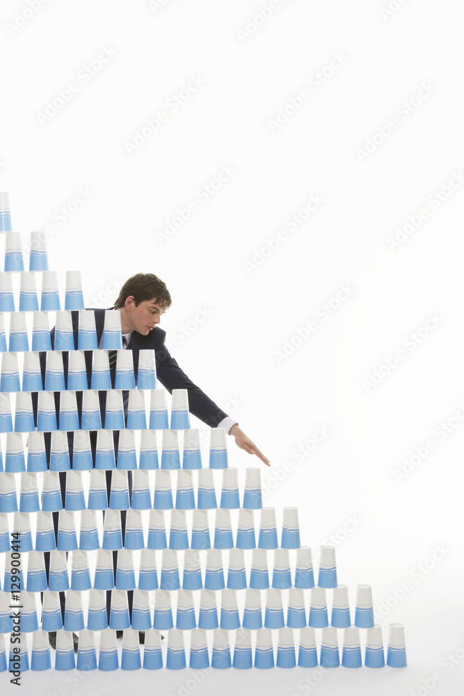 Young businessman stacking plastic cups into a pyramid against white background