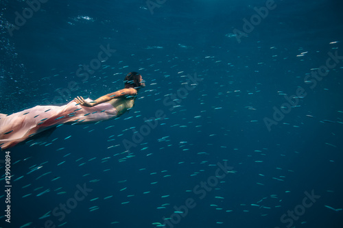 A model underwater in golden pink dress surrounded by small fish