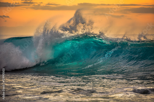 Green blue ocean splashing wave in front of orange sunset sky background © willyam