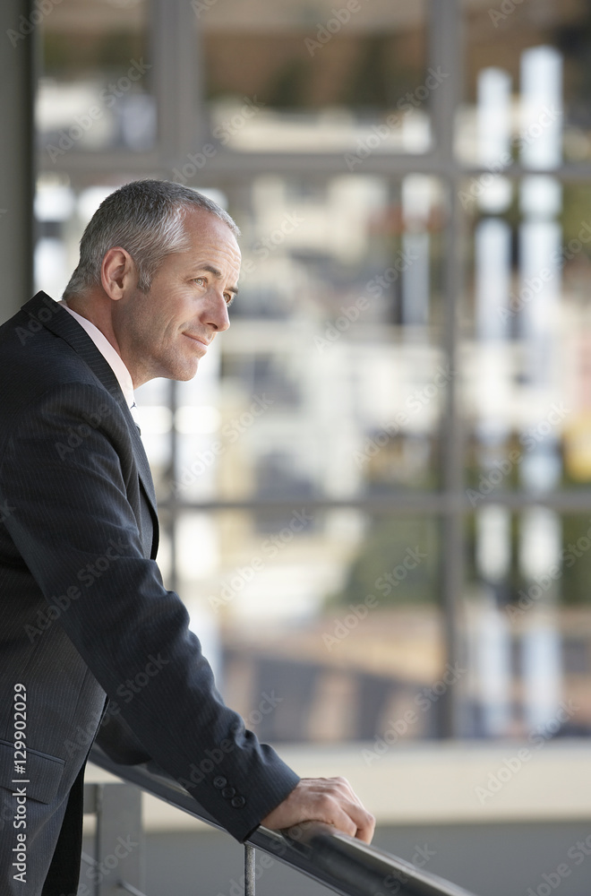 Side view of middle aged businessman leaning on railing in office