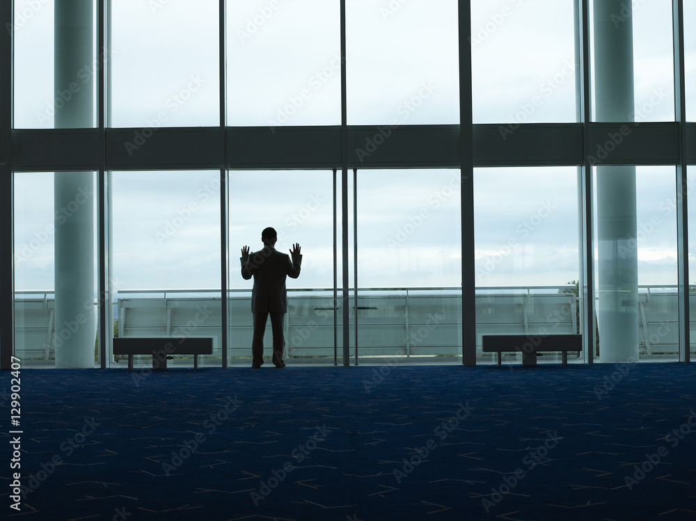 Rear view of a silhouette businessman looking out window at the airport lobby