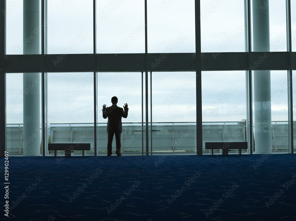 Rear view of a silhouette businessman looking out window at the airport lobby Rear view of a silhouette businessman looking out window at the airport lobby