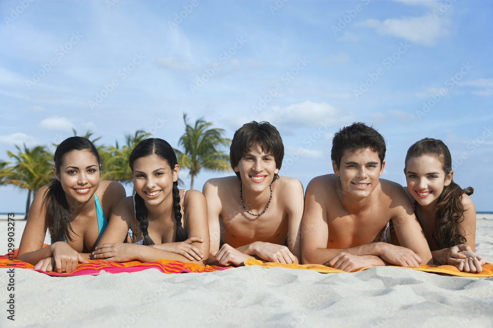 Portrait of happy teenage friends lying in row on beach towels Portrait of happy teenage friends lying in row on beach towels