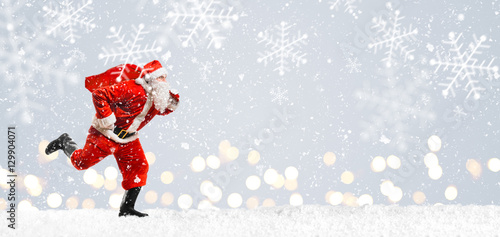 Santa Claus running at New Year or Christmas delivery rush with gift bag full of presents on snow