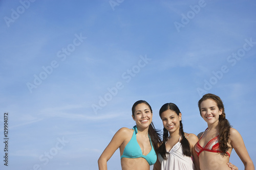 Portrait of happy teenage girls in bikinis standing against sky