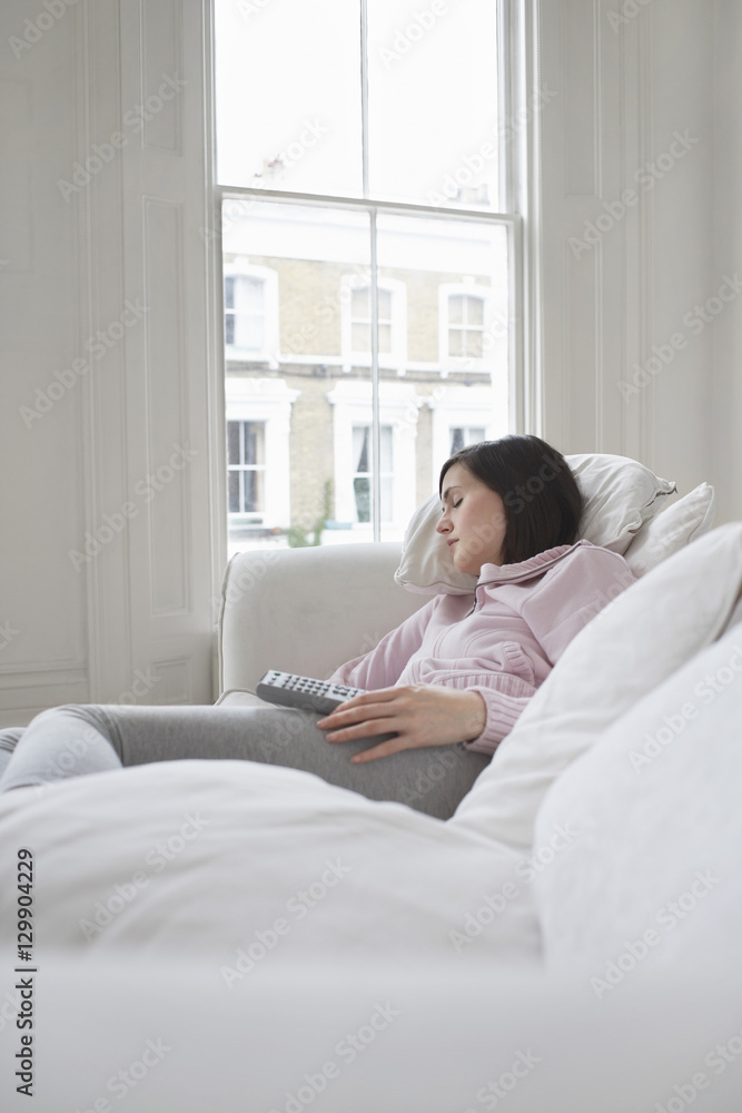 Young woman sleeping on couch with remote control in hand Young woman sleeping on couch with remote control in hand