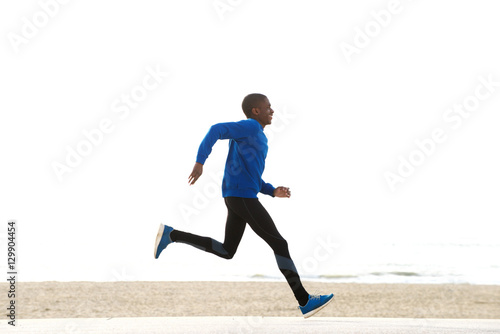 side portrait of young african american man running by the beach © mimagephotos