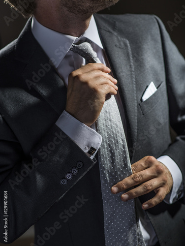 Obraz na plátně Sharp dressed businessman adjusting his necktie