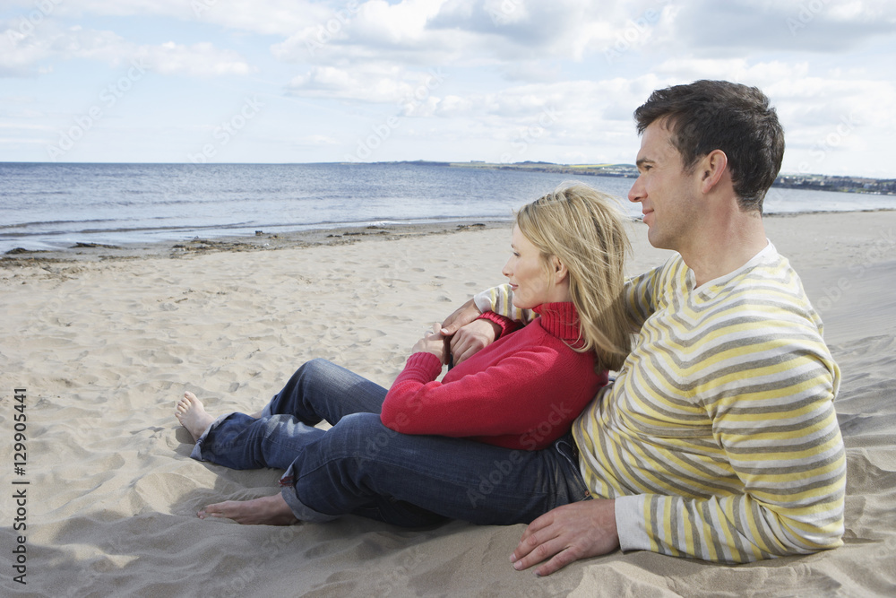 Side view of happy loving couple relaxing on sandy beach looking at ocean view