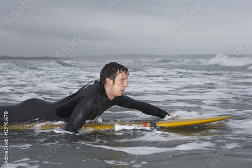 Side view of male surfer paddling on surfboard in water at beach