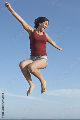 Low angle view of a young woman jumping in air against blue sky
