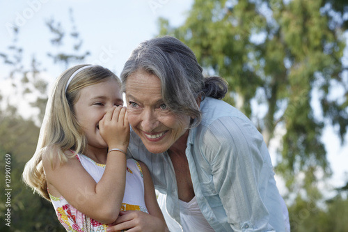 Closeup of a young girl whispering in grandmother's ear outdoors photo