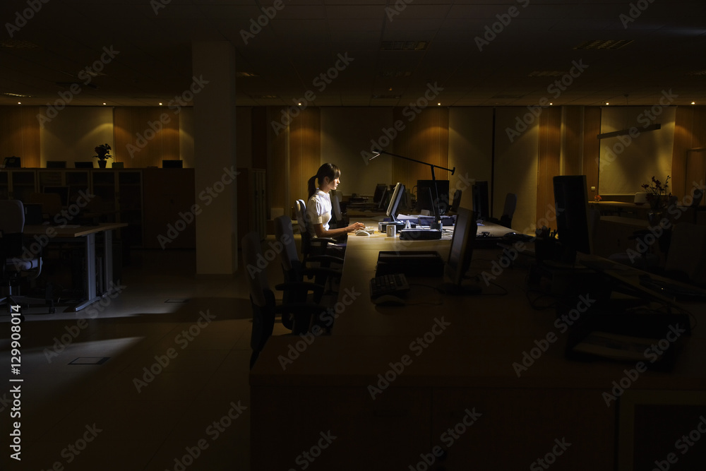 Side view of a young woman working on computer in dark office
