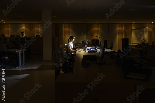 Side view of a young woman working on computer in dark office photo