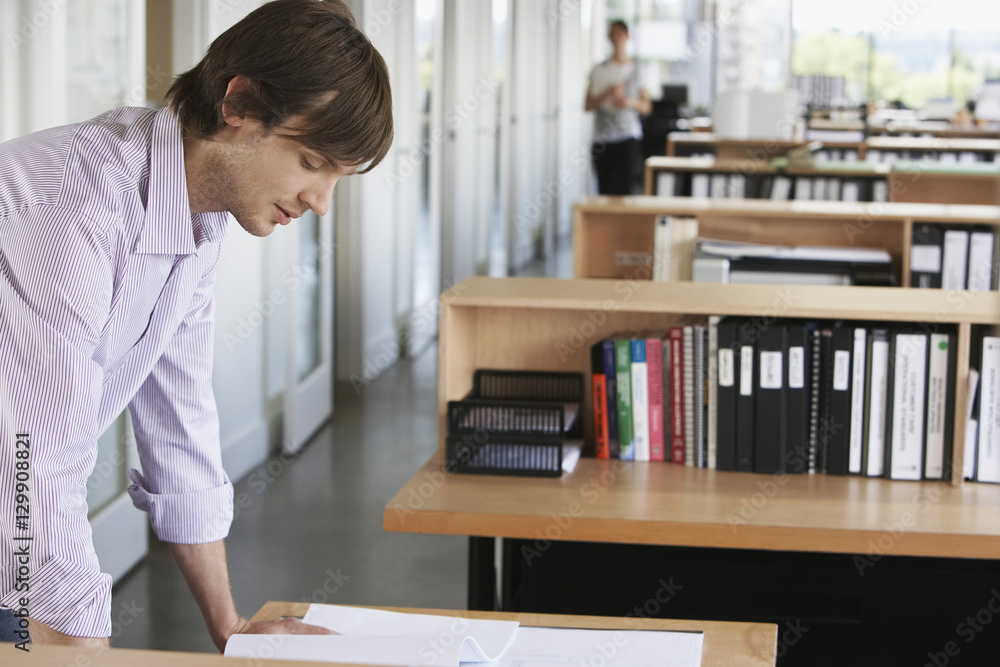Side view of a young male architect studying blueprint in office Side view of a young male architect studying blueprint in office