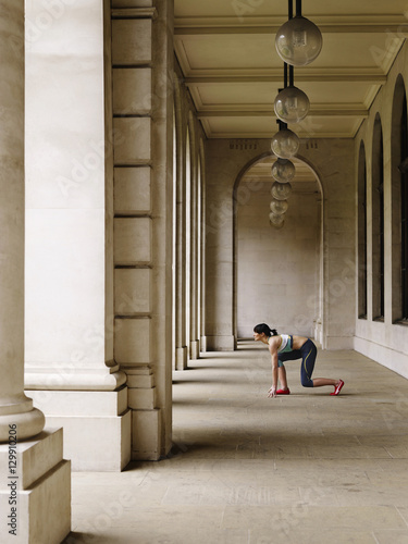 Full length side view of a female runner crouching in starting position in portico