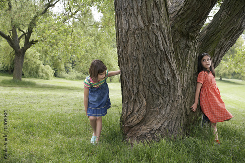 Full length of two girls playing hide and seek by tree