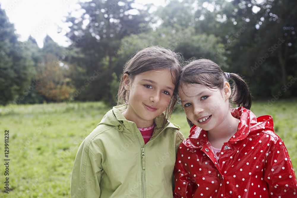 Closeup portrait of two smiling young girls in raincoats on meadow Closeup portrait of two smiling young girls in raincoats on meadow
