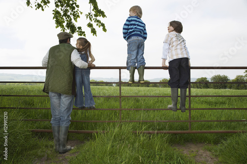 Full length rear view of father with three children looking at lush landscape by fence