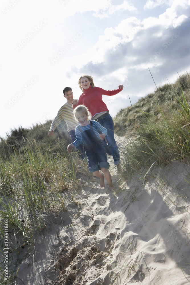 Full length of parents and daughter running through sand dunes on beach