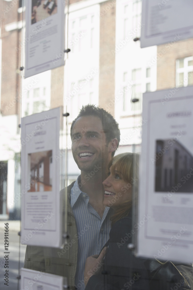 Fototapeta premium Closeup of a cheerful young couple looking through window at estate agents