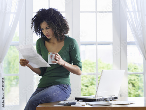 Canvas Print Displeased African American woman reading document with a coffee cup on desk